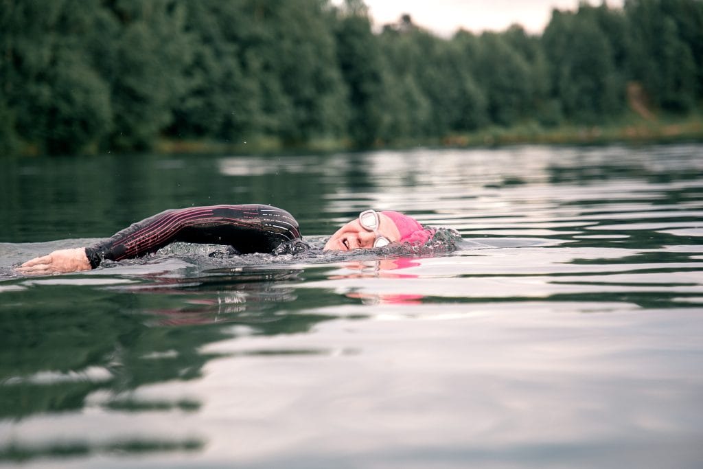 A woman athlete in a pink cap floats on the lake. Sports swimming triathlon. Wild Swimming_Devon